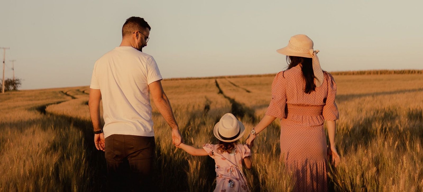 A family walking hand in hand through a wheat field at sunset