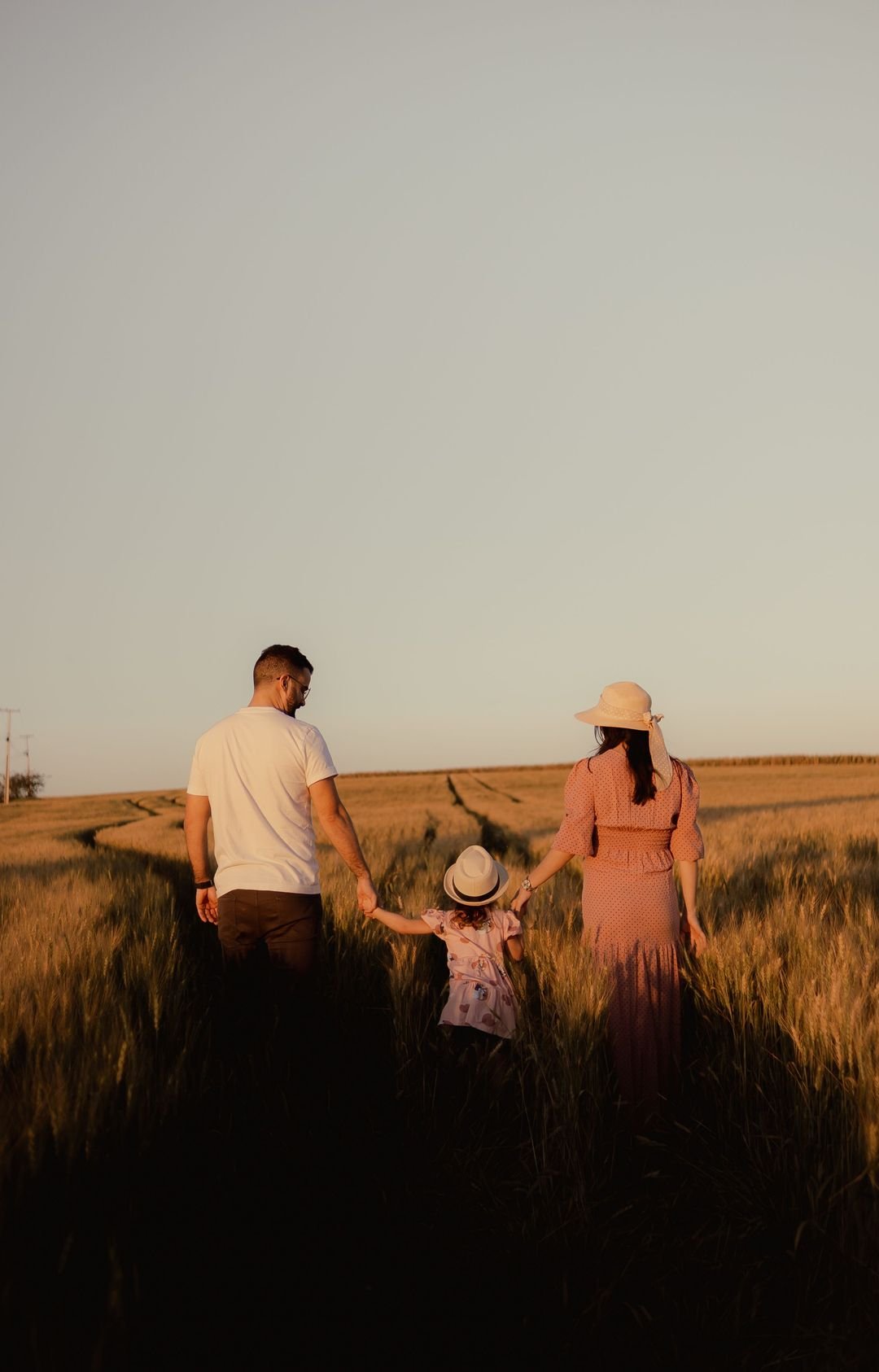 A family walking hand in hand through a wheat field at sunset